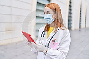 Young caucasian woman doctor wearing medical mask using touchpad at hospital