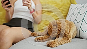 Young caucasian woman with dog holding cup a coffee using smartphone sitting on the sofa at home