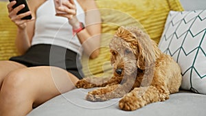 Young caucasian woman with dog holding cup a coffee using smartphone sitting on the sofa at home