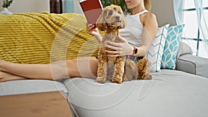 Young caucasian woman with dog reading book sitting on sofa at home