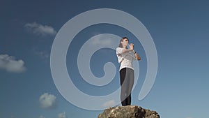 Young caucasian woman is doing yoga breathing and stretching exercises on rock on the beach