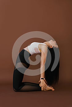 Young Caucasian woman doing yoga, stretching in the exercise is arranged, camel pose, workout, sportswear, white top and black tro