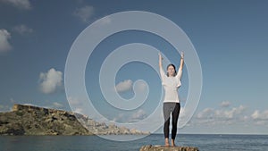Young caucasian woman is doing yoga and stretching exercises on rock on the beach