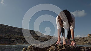 Young caucasian woman is doing yoga and stretching exercises on rock on the beach