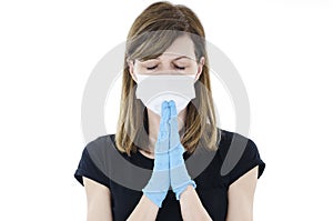 Young Caucasian woman dresses white facial medical mask, disposable gloves, wishing best, praying for sick people with coronavirus