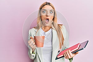 Young caucasian woman drinking a cup of coffee and holding laptop afraid and shocked with surprise and amazed expression, fear and