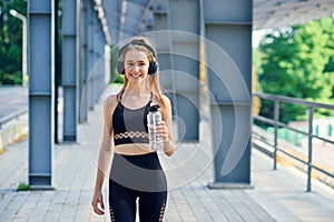 Young caucasian woman drinks water and listen to music after training.