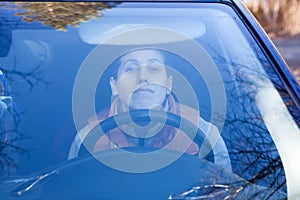 Young Caucasian woman a driver sitting in car and looking through the window, holding steering wheel