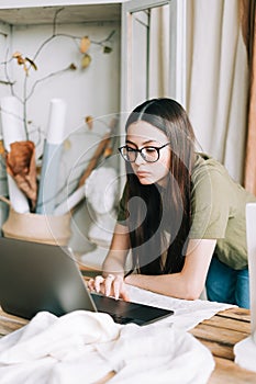 Young caucasian woman in eyeglasses working on laptop computer in home art studio