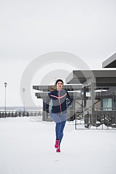 Young caucasian woman fitness model running at snow winter park - sport background