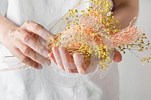 Young caucasian woman florist holds in hands bouquet of dry pink yellow decorative autumn flowers white wall background. Botanical