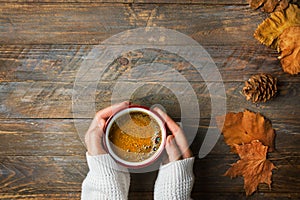 Young caucasian woman girl in knitted white sweater holds in hands mug with freshly brewed coffee dry orange leaves on wood