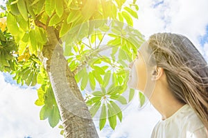 Young Caucasian Woman Girl with Long Chestnut Hair Standing under tree looking up in the sky green foliage