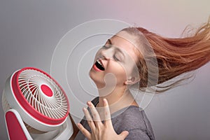 Young Caucasian woman girl with long hair holding electric fan in front her face. Cool down in hot summer weather concept
