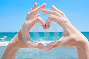 Young Caucasian Woman Girl Making Heart with Hands Palms. Turquoise Sea with Waves Blue Sky Horizon Background. Bright Sunlight