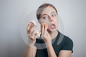 Young Caucasian woman girl is putting her make up powder foundation with funny face expression