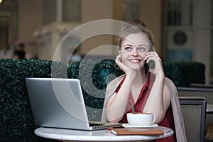 Young caucasian woman girl sitting in cafe with coffee and laptop and talking on the phone