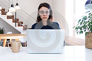 Young Caucasian woman with glasses working with laptop at home. Female freelancer using computer at office.