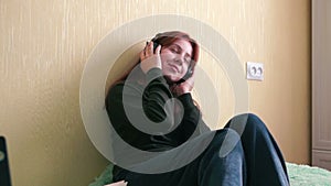Young caucasian woman in headphones sitting on the bed at home, listening to music, closing her eyes, enjoying listening to music,