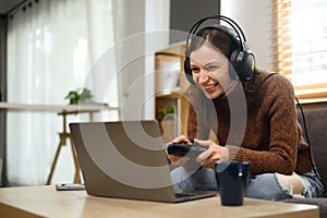 Young caucasian woman in headset holding joystick playing video game on laptop