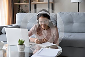 Young Caucasian woman in headset watch webinar making notes