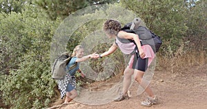 Young Caucasian woman helps her biracial friend up a steep trail