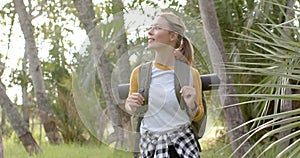 Young Caucasian woman hikes through a lush park, looking around with a smile