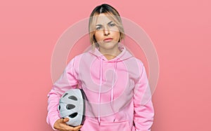 Young caucasian woman holding bike helmet thinking attitude and sober expression looking self confident
