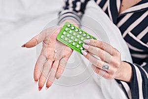 Young caucasian woman holding birth control pills at bedroom