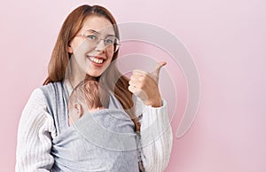 Young caucasian woman holding and carrying baby on a sling smiling happy and positive, thumb up doing excellent and approval sign