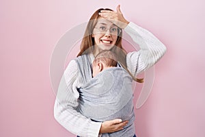 Young caucasian woman holding and carrying baby on a sling stressed and frustrated with hand on head, surprised and angry face