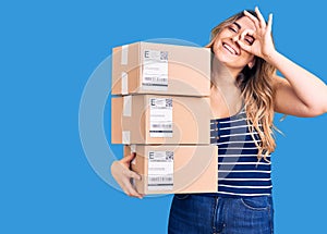 Young caucasian woman holding delivery package smiling happy doing ok sign with hand on eye looking through fingers