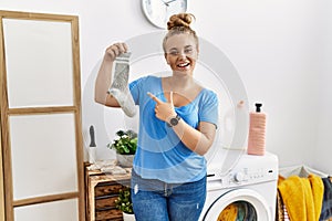 Young caucasian woman holding dirty sock at laundry room cheerful with a smile on face pointing with hand and finger up to the