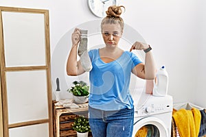 Young caucasian woman holding dirty sock at laundry room pointing down looking sad and upset, indicating direction with fingers,