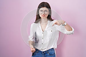 Young caucasian woman holding laptop pointing down looking sad and upset, indicating direction with fingers, unhappy and depressed