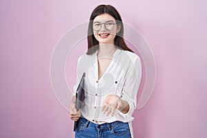 Young caucasian woman holding laptop smiling cheerful offering palm hand giving assistance and acceptance