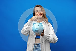 Young caucasian woman holding a piggy bank.against blue background