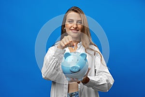 Young caucasian woman holding a piggy bank.against blue background