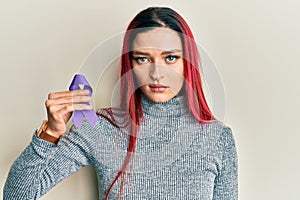 Young caucasian woman holding purple ribbon awareness thinking attitude and sober expression looking self confident