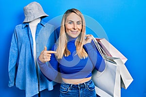 Young caucasian woman holding shopping bags pointing finger to one self smiling happy and proud