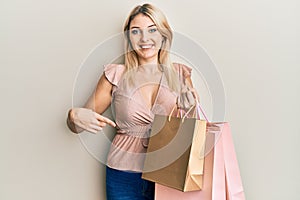 Young caucasian woman holding shopping bags smiling happy pointing with hand and finger