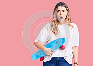 Young caucasian woman holding skate scared and amazed with open mouth for surprise, disbelief face