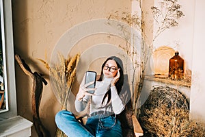 Young caucasian woman holding smartphone looking on cell using mobile phone technology at home