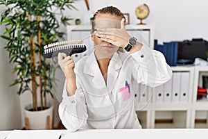 Young caucasian woman holding teeth whitening palette covering eyes with hand, looking serious and sad