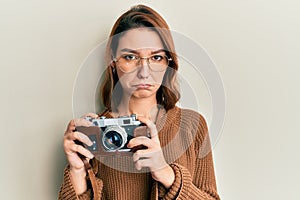 Young caucasian woman holding vintage camera depressed and worry for distress, crying angry and afraid