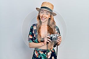 Young caucasian woman holding vintage camera looking positive and happy standing and smiling with a confident smile showing teeth