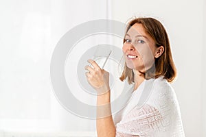 A young Caucasian woman holds a glass of water in her hand. White background. Copy space. The concept of healthy nutrition and