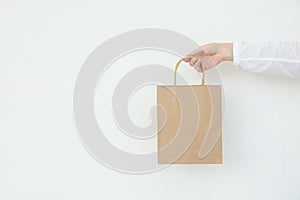 Young caucasian woman holds in hand empty blank mock up brown craft paper bag on white wall background. Christmas New Years