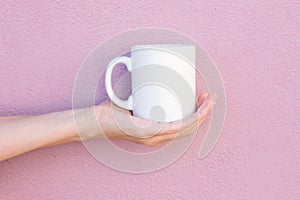 Young Caucasian Woman Holds on Hand Palm Blank Mockup White Mug on Light Pink Painted Wall. Airy Breezy Style