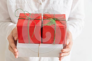 Young Caucasian woman holds in hands stack of gift boxes in white red paper with green twine. Christmas New Years presents